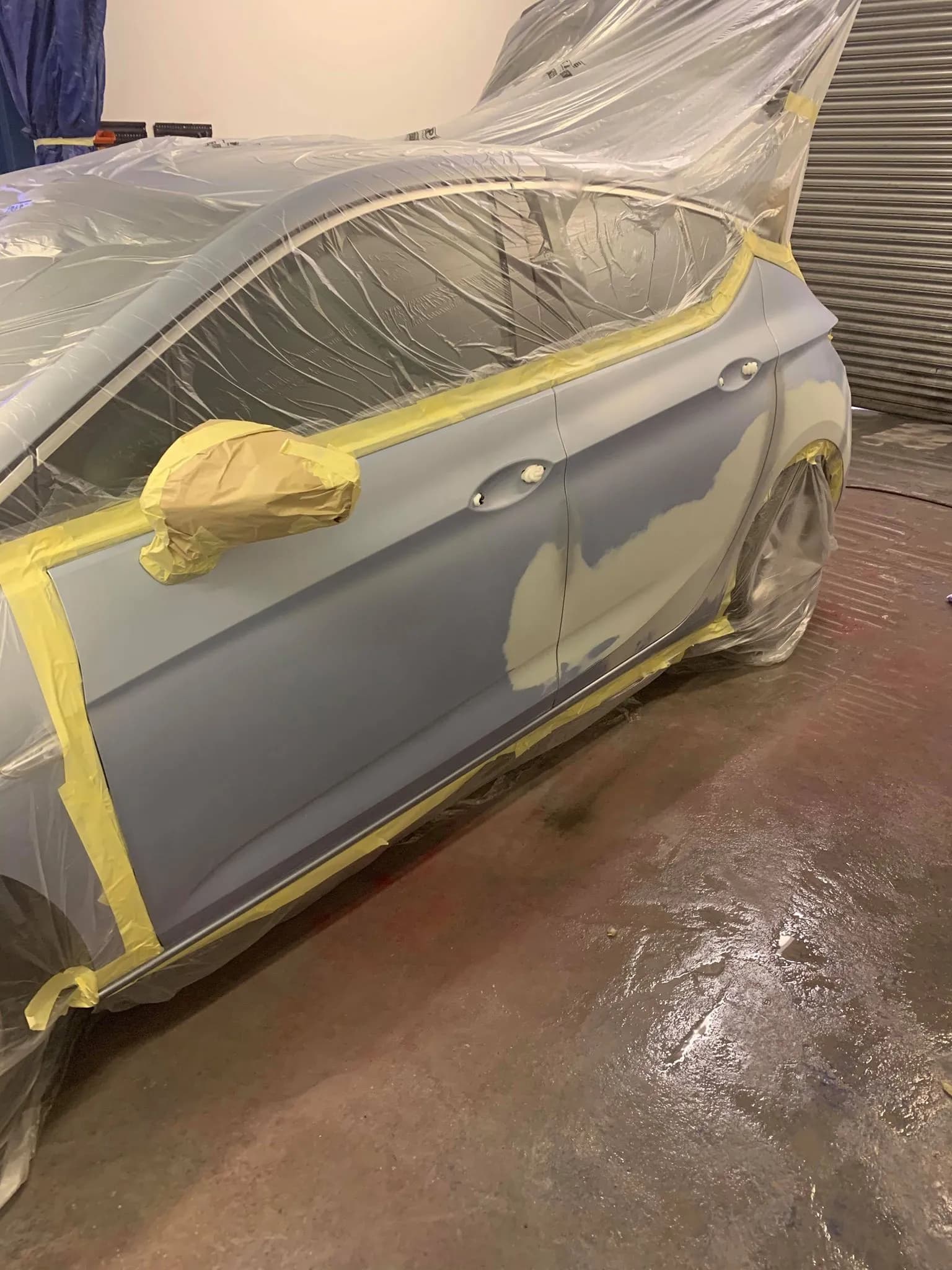 A car door in the workshop with a repaired area in primer, masked up for paint