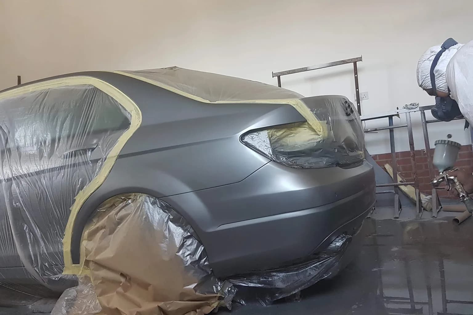 A grey saloon in the spray booth at Chattisham, masked with paper and film, being sprayed on the rear quarter